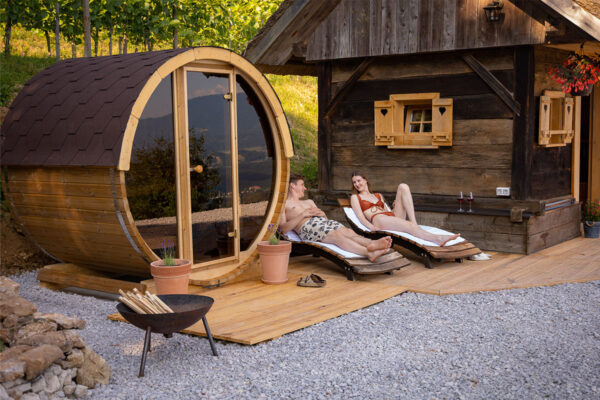 neptune-saunas-and-hot-tubs---customer-photo---Slovenia-2-person-barrel-suana-with-couple-enjoying-the-sun-loungers-next-to-it