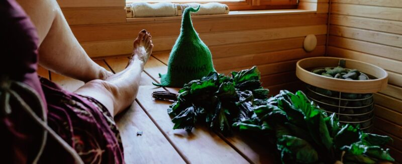 Neptune Saunas Blog - woman relaxing in sauna with a whisk and sauna hat on the bench