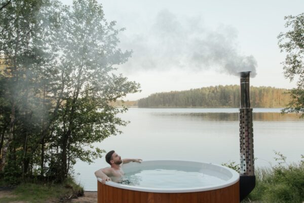 Neptune blog article on hot tub health benefits - man bathing in a wood fired tub in the wilderness by a lake